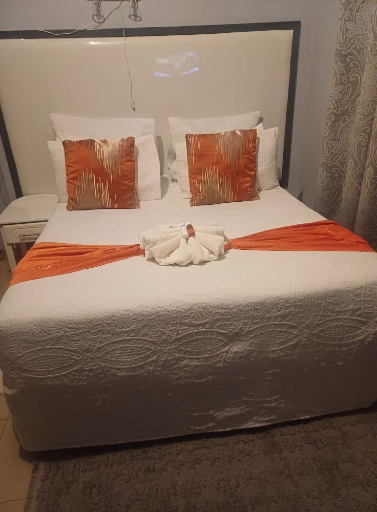 A Bulawayo bedroom with a white bed, orange cushions and a runner with a folded towel swan