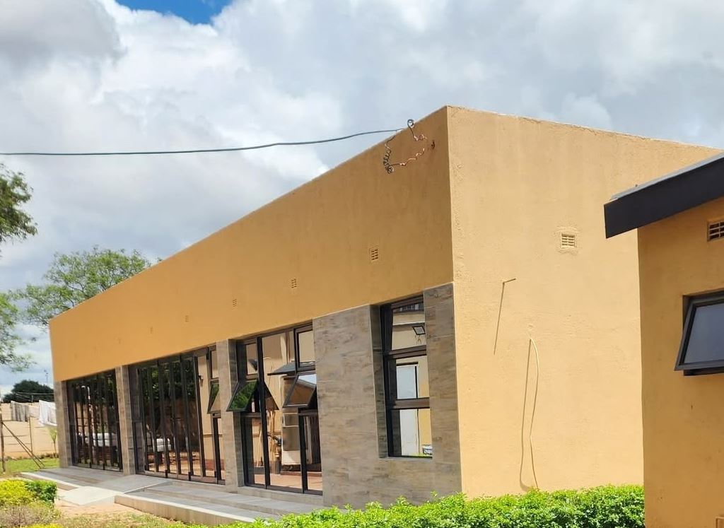 The single-storey ochre and stone Bulawayo lodge under a blue sky, with a trimmed hedge in front