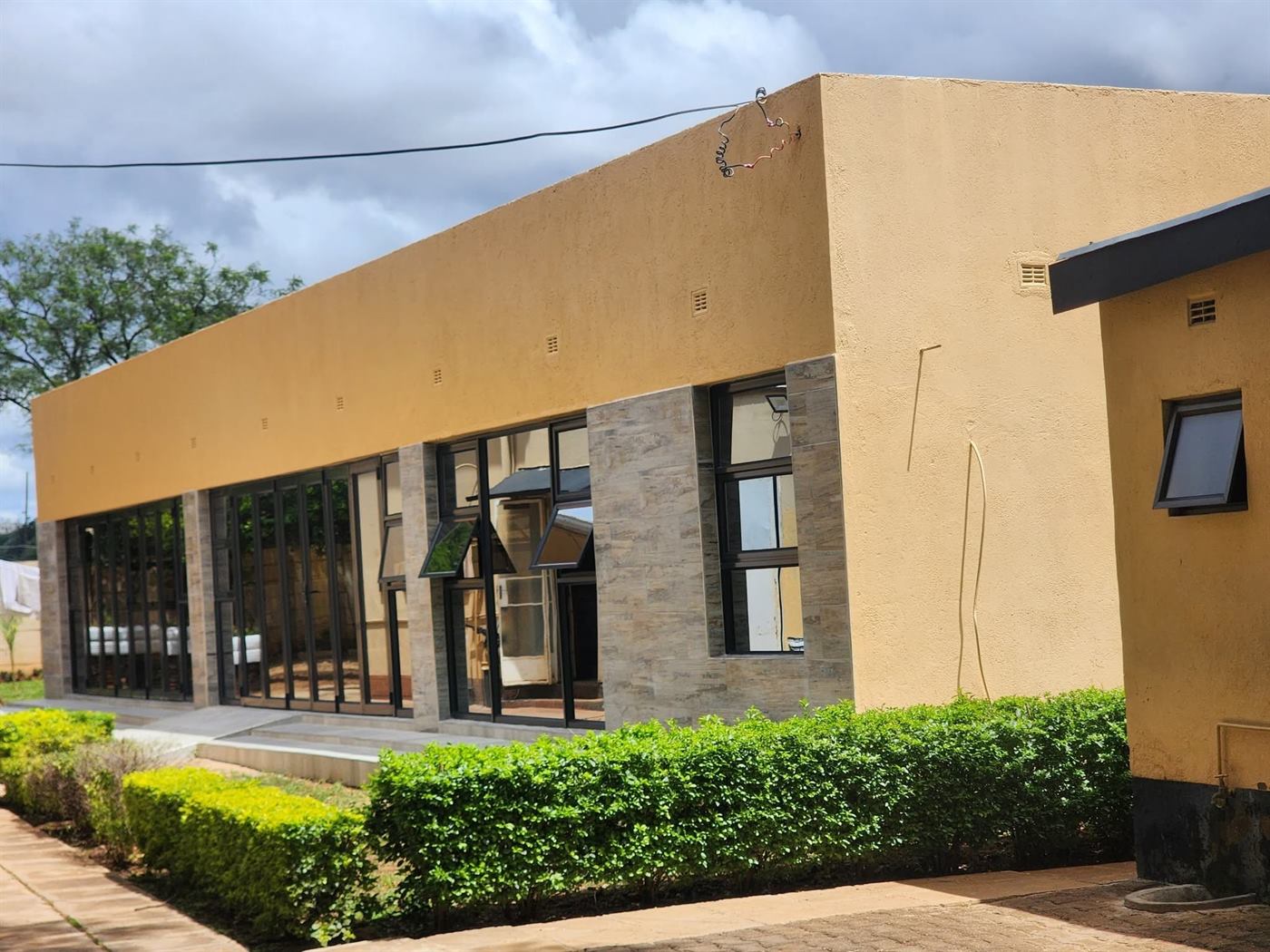 Front of the Bulawayo lodge: ochre walls, stone cladding and glass doors behind a green hedge