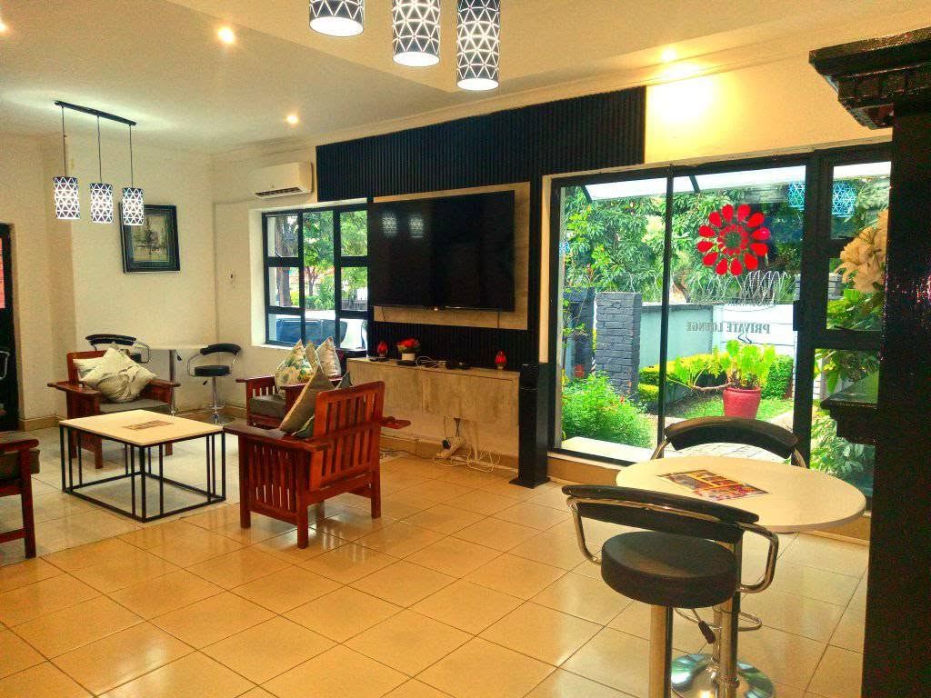 The Bulawayo lounge with wooden chairs, a wall-mounted TV and a glass door to the garden
