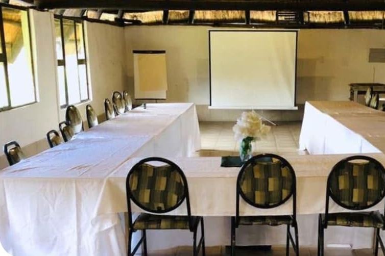 Harare conference room under a thatched roof, with a projector screen and white-clothed tables in a U shape
