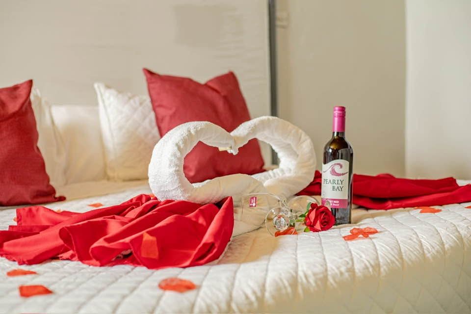 Bed with a folded towel swan, red cloth, red cushions and a bottle of wine